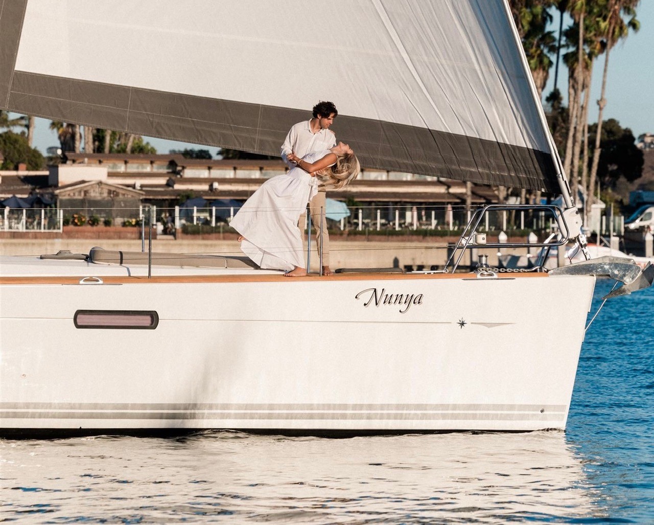 Side profile of the Jeanneau 51 yacht Nunya sailing during golden hour with San Diego skyline behind